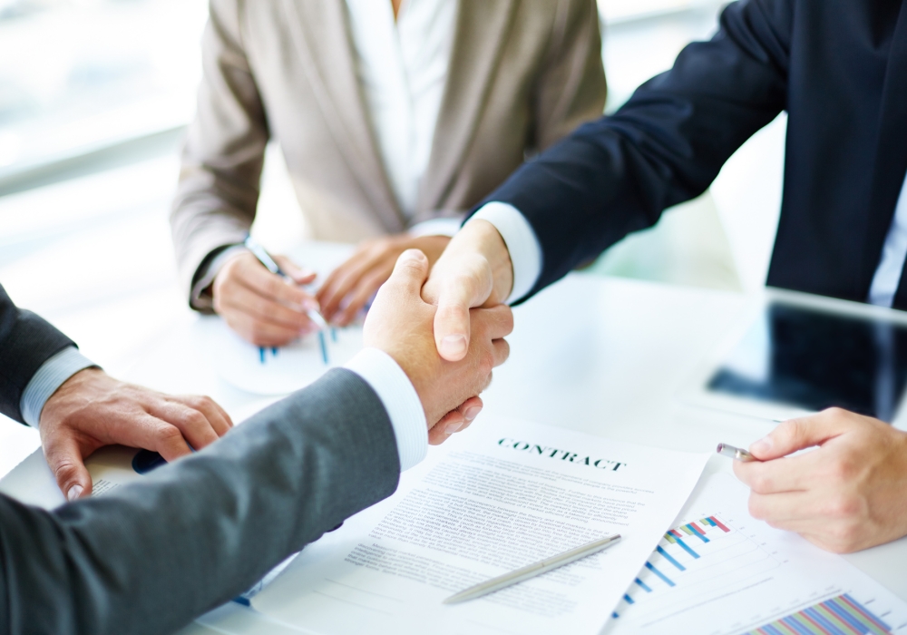 Making agreement Image of business partners handshaking over business objects on workplace